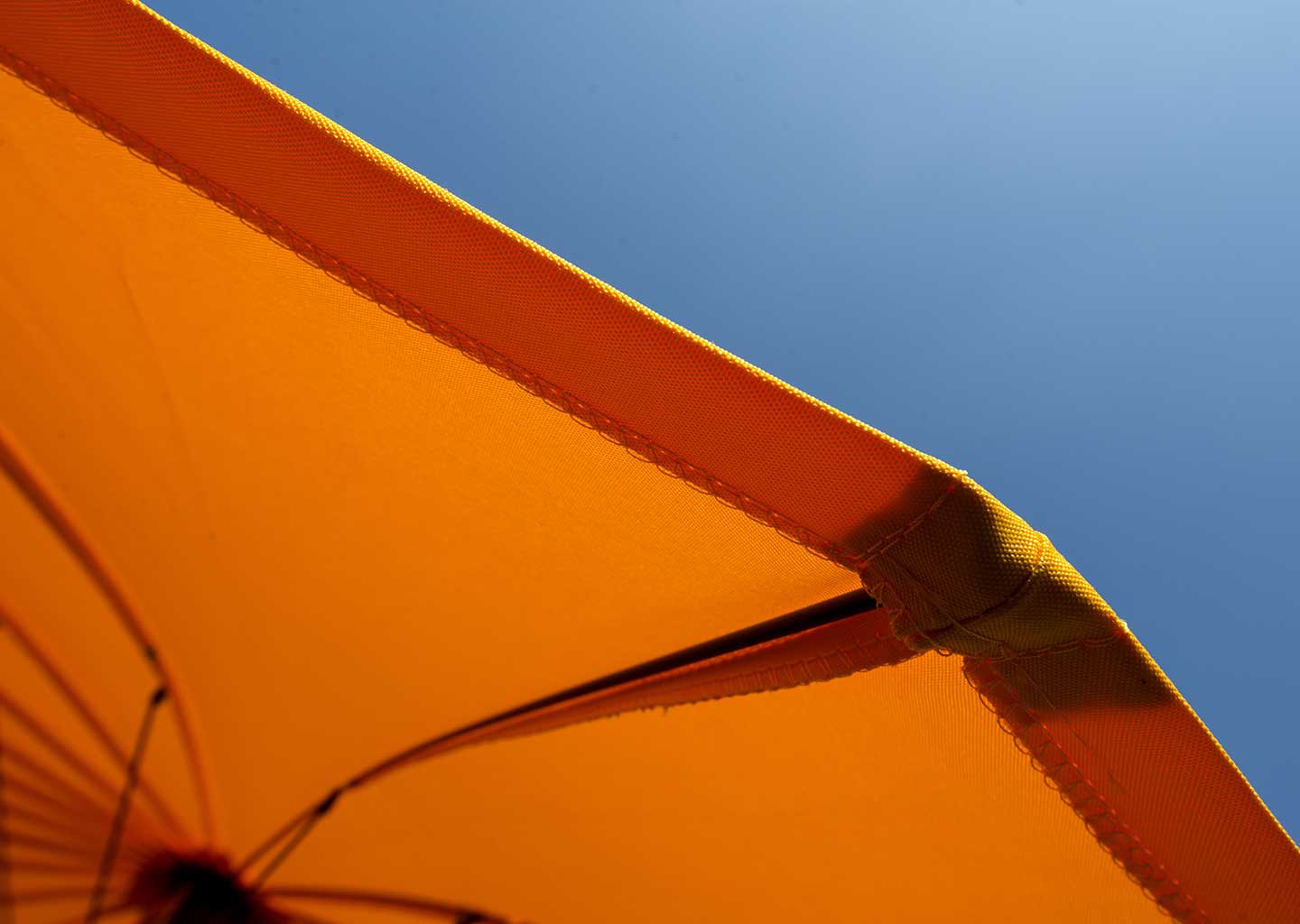 UV-Schutz bei Textilien: Orangener Sonnenschirm vor hellblauem Himmel.